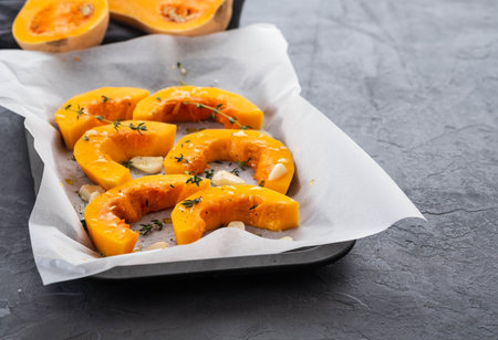 Sliced pumpkin with greens and sea salt on white baking paper as background. Top view. Copy space.の写真素材