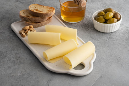Cheese slices on white board with honey, figs, olives, grapes.