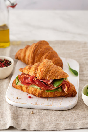 Fresh croissant or sandwich with cucumber, ham, Jamon, prosciutto, on wooden background. Morning breakfast concept. Healthy and fast food.の写真素材