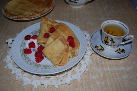 Pancakes with raspberries and sour cream lie on a plate which stands on a white napkin next to it is a cup of black teaの写真素材