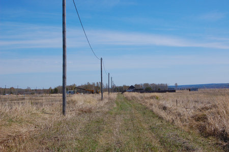 the road is in the field, there is a construction equipment and house n the distanceの写真素材