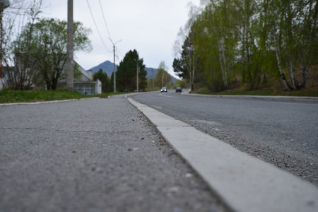 concrete road, 2 cars are driving in the distance, trees are growing, there is a building, there are electric polesの写真素材