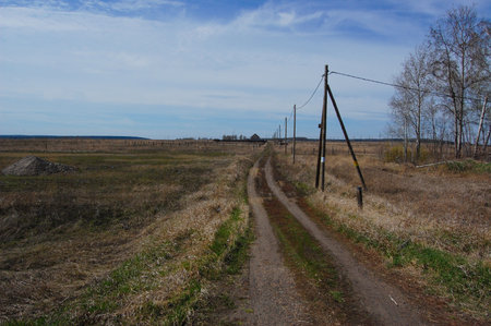country road with electricity poles, pile of gravel, houses in the distanceの写真素材