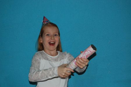 a little girl with red hair in a white blouse on a blue-gray background blows up a cracker and rejoicesの写真素材