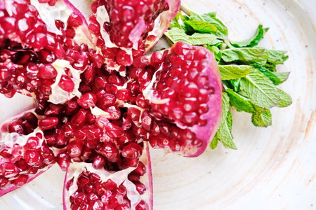 a red pomegranate cut into pieces is lying on a white plate decorated with mint sprigs.の写真素材