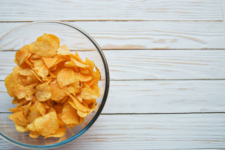 chips in a glass cup on a white wooden backdrop, harmful food.