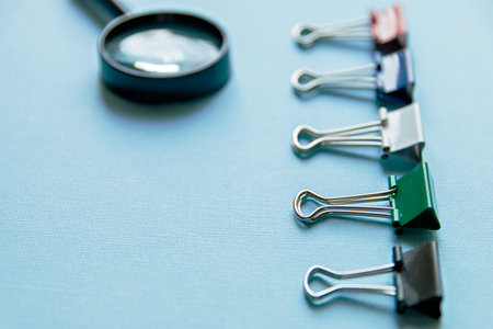 A magnifying glass and colored paper clips on a blue backgroundの写真素材