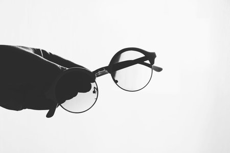 round glasses in a female hand on white interspersed background.