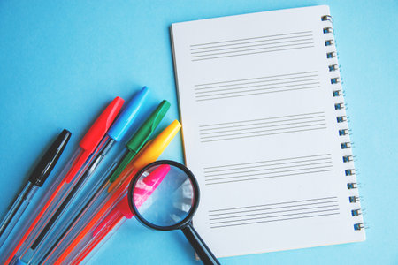 colored pens and magnifier on a white sheet of notepad for text.の写真素材