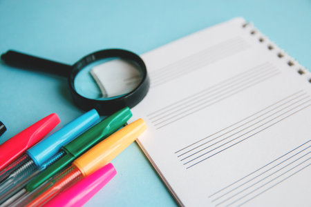colored pens and magnifier on a white sheet of notepad for text. Education or business concept.の写真素材