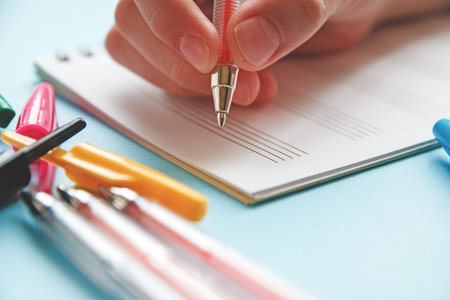 child s hand holds red pen in hand to make note in notepad.の写真素材