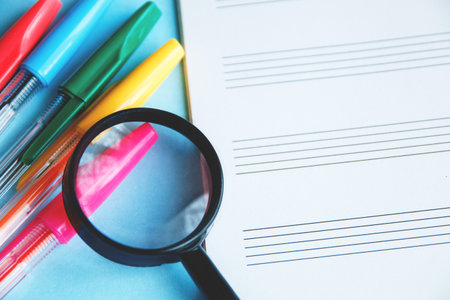 colored pens and magnifier on a white sheet of notepad for textの写真素材