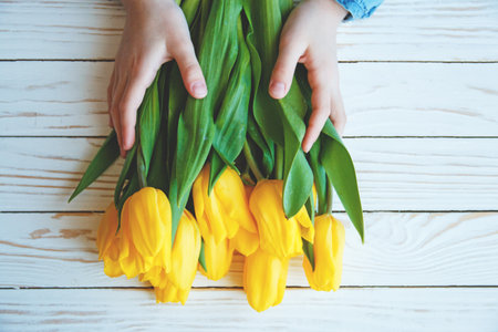 child hands hold bouqet of yellow tulips on a white wooden background.の写真素材