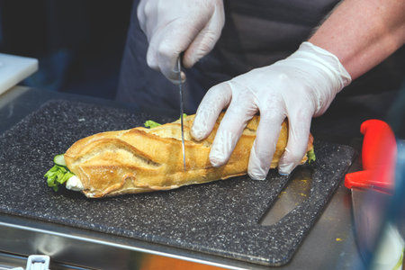 cook in disposable gloves cuts sandwich.の写真素材