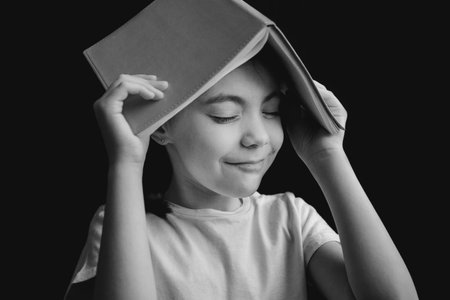 pretty cute girl white t-shirt with copybook in the form of a roof on black background. black and white image.の写真素材