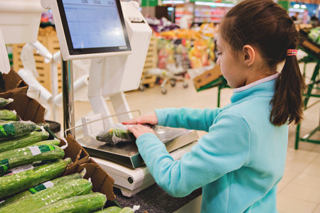 girl weighs fresh cucumbers on scales at the store.
