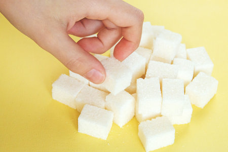 children's hand takes the white refined sugar randomly scattered on yellow background.の写真素材