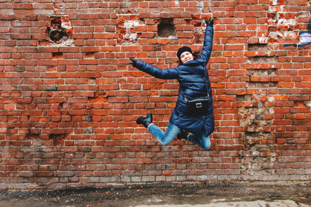 smiling girl was photographed in a jump on a brick wall background.の写真素材