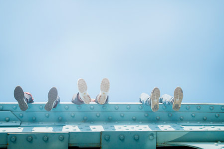 legs in sneakers hang from the bridge above in sunlight.の写真素材