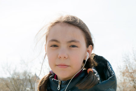 schoolgirl with backpack in warm sunny weather on the street with headphones listening to music in the gadget.の写真素材