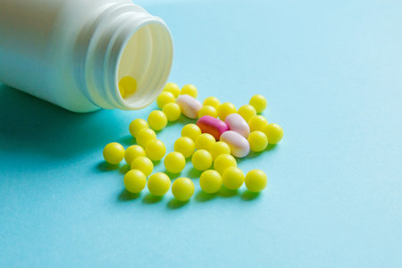 random yellow and pink pills in white bottle on blue isolated background.の写真素材