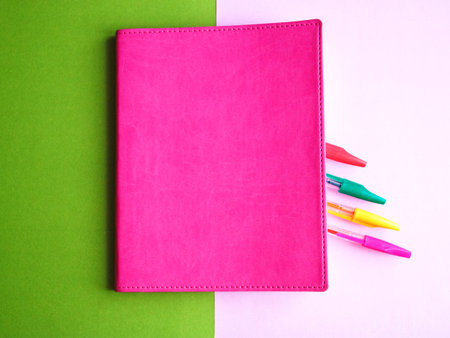 colorful pens in pink notebook on green and pink background, education concept.の写真素材