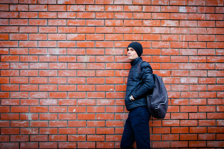 a young man stands leaning against a brick wall waiting for something.の写真素材