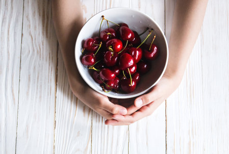 delicious ripe cherry in a bowl in children's hands on white wooden background.の写真素材