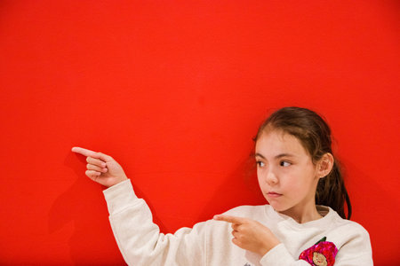 small girl pointing away at copy space with two fingers isolated over red background.の写真素材