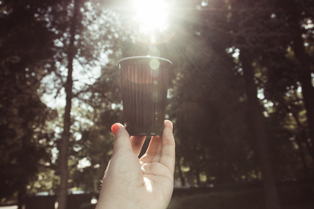 a glass of water in a woman's hand against the forest with the sun.の写真素材