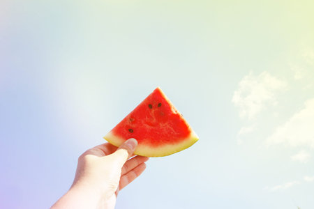a piece of ripe watermelon in hand against the blue sky.