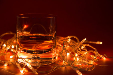 a glass of whiskey and in the background a glowing garland on a red background with a copy of space.