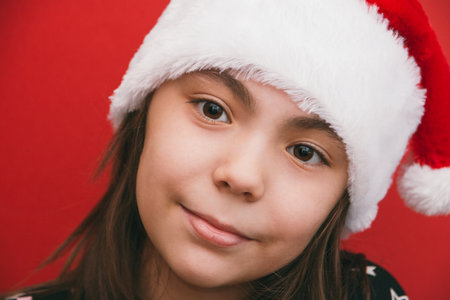 Cute little girl in Santa Claus hat on red backgroundの写真素材