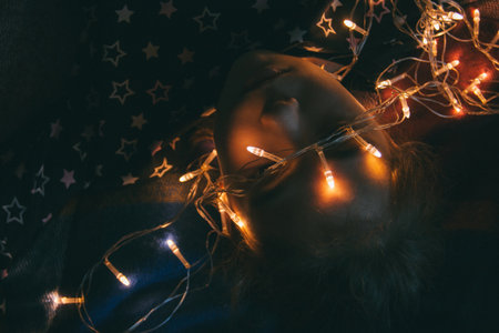 smiling happy girl lying on a blanket with a glowing garland focus on a garland.の写真素材
