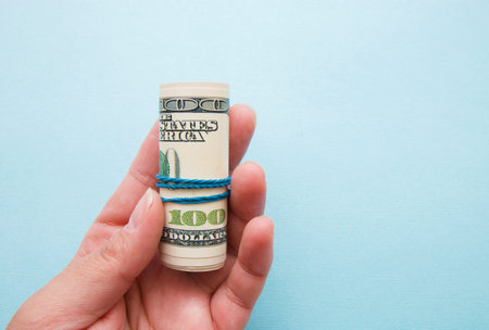 dollar money rolled into a pipe in a woman's hand on a blue background.