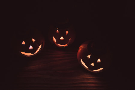 three glowing pumpkin faces for Halloween on wooden background. the symbol of Halloween.の写真素材