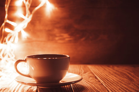 a Cup of coffee on a wooden background in the background garland.の写真素材