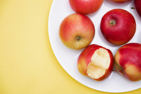 several whole red apples and one bitten in a plate on a yellow background of autumn composition and...