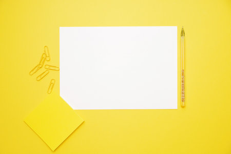 pen white paper yellow stickers and clips on yellow background with copy space top view.の写真素材