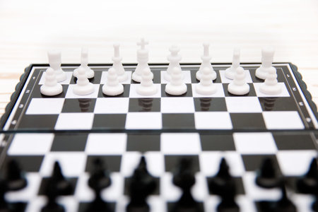 small pocket chess, plastic chess pieces placed on a chessboard on a white wooden background.