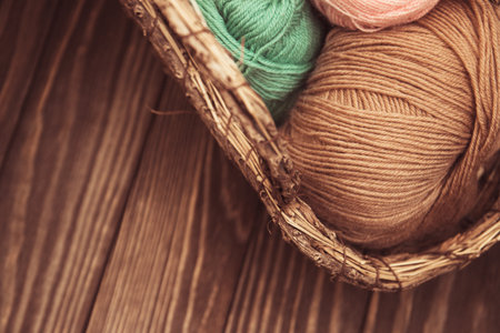 top view of brown and green woolen tangles of threads in wicker basket on wooden knitting background.の写真素材