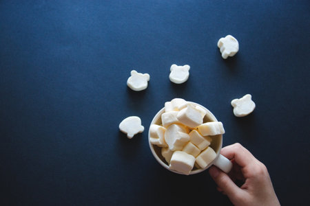 marshmallow in the form of bears in a white cup holds a hand on a dark background.の写真素材