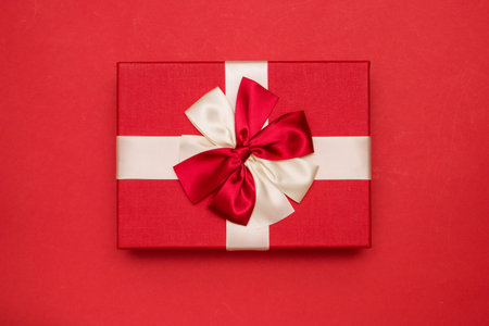 Real box with white and red bow and ribbon top view on Valentine's day isolated on red background....