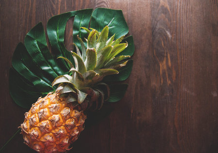 Pineapple and green leaf of monstera tree on wooden background top of view, selective focus.