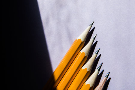 five simple pencils on a solid purple background in hard sunlight contrasting light from the window with a copy space.の写真素材