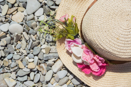 Wicker beach baby hat with flowers on the beach. Seashore with pebbles.
