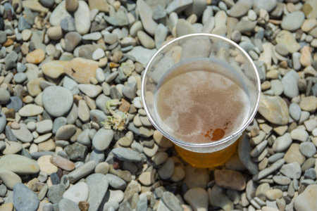 Plastic glass of light cold beer on the beach. Seashore with pebbles.