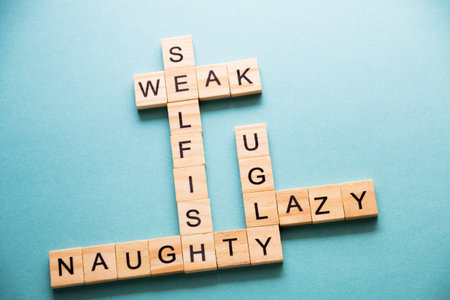 weak, selfish, ugly, mischievous, lazy words are collected in a crossword puzzle with wooden cubes on a blue background.の写真素材