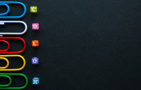 multi-colored paper clips and word color with small cubes on dark background, stationery.の写真素材