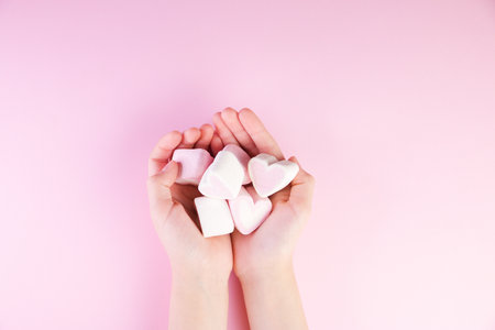 Pastel valentine background made of marshmallows souffle in the form of hearts on a pink background in hands. Valentine's Day concept with copy space.の写真素材